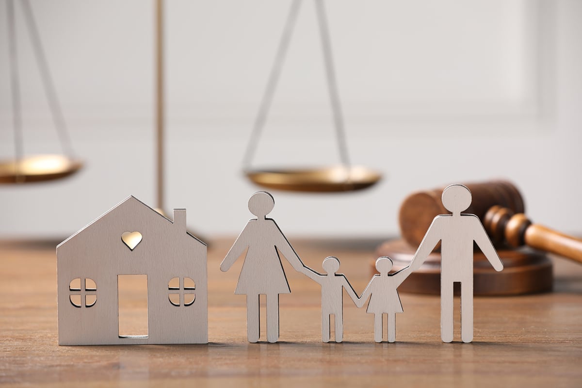 Navigating the Real Estate Landscape: This image, featuring a wooden house cutout and a family against the backdrop of legal scales and a gavel, visually represents the journey towards homeownership amidst evolving legal matters and changes in the real estate market. It underscores the article's focus on understanding and adapting to the current real estate environment to achieve homeownership goals with buying or selling.